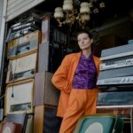 A Woman in Orange Blazer Standing Beside Vintage Radio