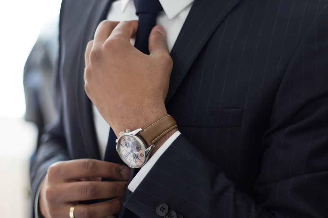 Adjusting the tie by Audio Brands man wearing watch with black suit